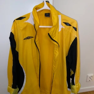 vindjacka - En gul vindjacka , använd fåtal gånger men köpt secondhand. Är i bra skick, förutom en fläck på ena armen som ej går bort. (Se sista slide) 