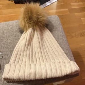 Vit mössa med pälsboll - Så fin vit mössa med en fake pälsboll upptill! Använt en del men fint skick. Frakt ingår ej.