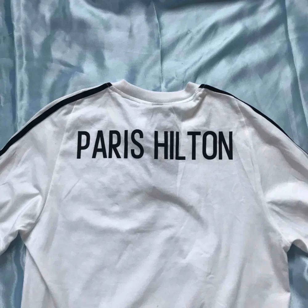 Helt oanvänd Adidas-tröja med ”Paris Hilton” tryckt på ryggen. Frakt betalas av köparen 🌸. T-shirts.