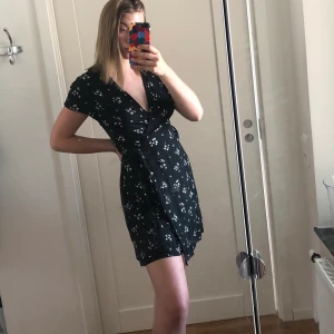 svart sommar klänning  - en kort sommar klänning med blommor på, kortärmad och knytning i midjan. Knappt använd, jätte fint skick, jag är 177cm lång och klänningen slutar mitten på mina lår. Frakt ingår ej, kan mötas upp i karlstad :)