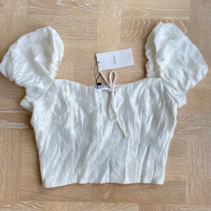Crop top med puffärmar - Crop top i glansigt/skimmrigt material med puffärmar från Bershka. Helt oanvänd med prislapp kvar. Strl L, men liten i storleken så passar mer en M. Säljes för 100kr eller bud om flera är intresserade.