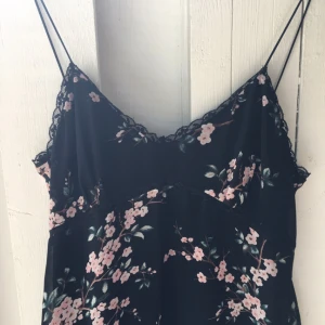  - Klänning svart med rosa blommor spets i över och underkant.  Även spets i avskärningen under byst. Chiffong ytter och fodrad. 