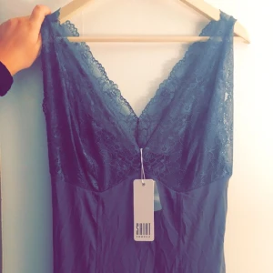  - NU 100kr (-100kr) + ev frakt  Figurnära mörkgrå klänning med djup v-ringning vid byst & rygg. Spetsen är mjuk & tyget är elastiskt.  Snygg både som nattlinne & till fest med ex. kimono & klackar! Strl. L  Aldrig använd!