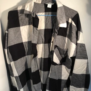 Flanellskjorta  - Snygg flanellskjorta i svartvit från mobil! Denna är riktigt härlig och snygg men passar tyvärr inte riktigt mina til längre och därför säljer jag den. Det är i nästan nyskick! Kan mötas upp annars tillkommer frakt