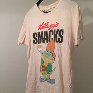  - Naturfärgad T-shirt med "Kelloggs" tryck från Pull & Bear. Är en herrskjorta i storlek M (38) men passar nog en Large också! Frakt eller upphämt