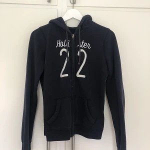 Hoodie Hollister - En väldigt fin marinblå hoodie från Hollister som är i fint skick! Siffrornas tråd är lite glittriga vilket jag tycker gör väldigt mycket på hoodien! 😍 Om ni har frågor eller funderingar så hör av er!  Frakt tillkommer! 
