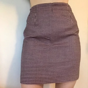 Kjol i hundtandsmönster - Kort kjol i svart/rosa hundtandsmönster. Passar storlek 36/38. Viss slitning bak, se bild. Syns ytterst lite i verkligheten. DM vid intresse eller för mer info.