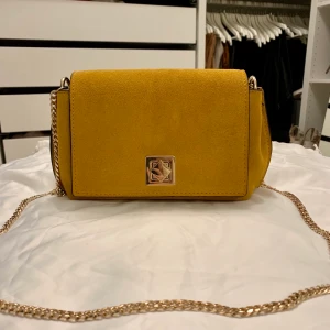 Den perfekta höstväskan! 🍂  - NY. Senapsgul mockaväska från Mango med guldkedja. Väskan är använd en gång, i toppskick! Rymlig med fack och dragkedja invändigt. Mått: 24x14 cm. 