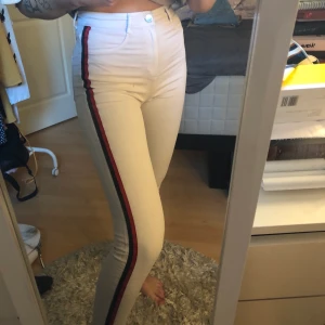 Vita jeans - Vita tighta jeans med en röd rand på sidan. Har slitningar längst ner på byxorna. Från Zara i storlek 36. Fint skick. Frakt tillkommer. Skicka meddelande för mer bilder