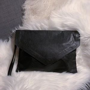 Wera clutch väska i skinn - Snygg clutch / kuvertväska i aningen oversized stil. Supersnygg att bära under armen och har även ett band att ha runt handleden. Fack med dragkedja och mobilfack inuti. Sparsamt använd, nyskick. Mått: 35x25cm