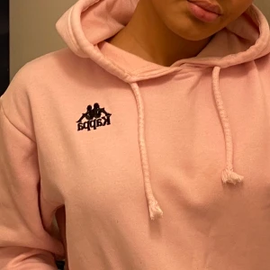 Kappa Hoodie  - Säljer min baby rosa super mysiga hoodie ifrån Kappa nyköpt för 600kr i London. Använd ett fåtal gånger dvs i bra skick, säljer den pga att den inte kommer till användning. I Stl M, bara att skriva för fler bilder/frågor. Köparen står för frakten. (Finns inga skador fläckar eller märken på hoodien det ser ut som det pga spegeln)