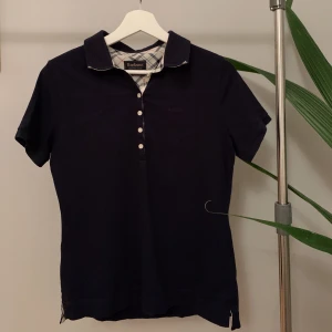 Barbour Piké - Säljer min piké från Barbour! Aldrig använd. Färgen är mörkblå med märket i samma färg. Fina detaljer på insidan av kragen samt under kragen. Materialet är 94% bomull och 6% elastan. Står att det är storlek 12 vilket kan vara svårt att tolka men skulle säga att tröjan passar en XS - S 