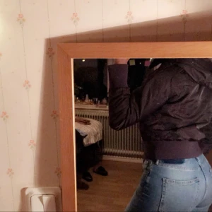  - Brun jacka med en luva.en svart blomma bakom.