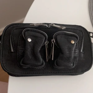 NuNoo - NuNoo väska i äkta läder. Mini versionen. Bredd: 19 cm, Höjd: 10 cm, Djup: 5 cm. Nypris 1099:-. Aldrig använd. Medföljer en silvrig kedja. 