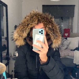 MONCLER JACKA - XS/S - Moncler jacka i svart med ÄKTA päls. Ganska tunn, passar till våren och hösten. Ganska kort, går ner till lite mindre än rumpan. Har ett bälte runt midjan med metall som man knäpper med Moncler logga, vilket ger en ”figurformad” jacka. Passar XS/S!