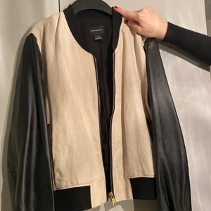 Club Monaco bomberjacka - En bomberjacka från Club Monaco (ägs av Ralph Lauren) i beige tyg, känns som linne tyg, med svarta ärmar i skinn. Storlek L men skulle säga att det är en M. Använd fåtal gånger.