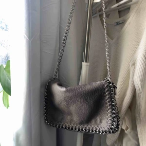  - Grå väska i skinnimitation med en silvrig kedja från märket tiamo. Längd 28cm, höjd 18cm, bredd 5cm och kedjan mäter 108cm. Nypris 499kr. Priset är exklusive frakt.💓