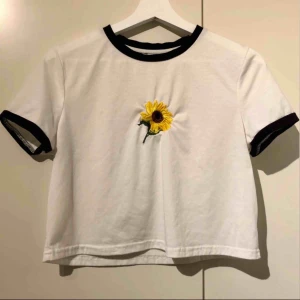  - Vit t-shirt med solros som motiv och svarta kontraster längs krage och ärmar! Härlig till våren och sommaren🤩 Frakt tillkommer!🌻