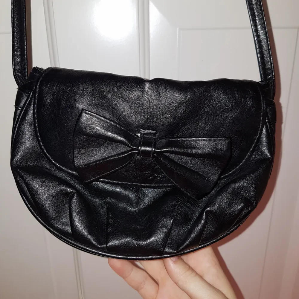 Skitsnygg svart väska med en rosett. Väldigt lång (axelbandetbandet ca. 60 cm) men praktisk pga hur liten den är! . Accessoarer.