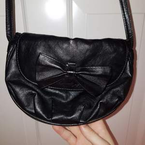 Skitsnygg svart väska med en rosett. Väldigt lång (axelbandetbandet ca. 60 cm) men praktisk pga hur liten den är! 