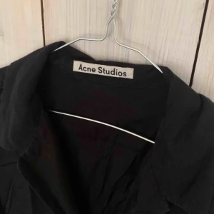  - Acne studios - Skjorta Nypris: 2999 kr. Mitt pris: 200 kr + 63 kr frakt. Storlek: 38  Svart skjorta från Acne. Använd fåtal gånger men har tyvärr en liten defekt på vänster sida i form av ett litet hål. Se bild nedan.