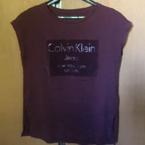 Calvin Klein  - Plommonfärgad T-shirt med loggan i typ sammetstryck (se mittenbild). Använd o välvårdad. Säljer den för jag trivs inte riktigt bra i den. Köpare betalar frakt 