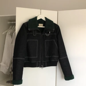 Jacka med detaljer - En svart/mörkgrå jacka i jeans material som är fodrar med grönt foder från Urban Outfitters. Har detaljer i vita sömmar och en krage. Knappt använd. 
