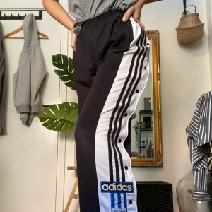 Adidas byxor - Säljer dessa adidasbyxor med adidasloggan + stripes på båda sidorna. Köpta second hand men knappt använda av mig, bra skick. Har två fickor med dragkedjor, har små slitningar på knapparna (se bild 2) men inget man tänker på. Förstår inte riktigt storleken men se bild 3 för lappen. Jag är vanligtvis en s/m till referens och de är ganska stora i midjan för mig men går att dra ihop med snöre som knyts på insidan. Buda i kommentarerna eller skriv privat om du har frågor💞