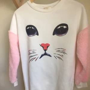  - Söt sweatshirt med pälsärmar och kattryck! Vita muddar. Tröjan är lite längre i modellen, slutar en bit ner på höften. 