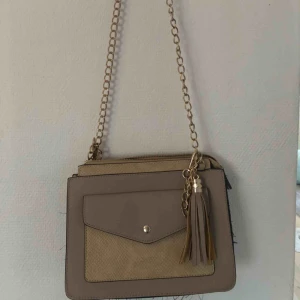  - En väska i beiget och ljusbrunt med guldiga detaljer. Märke okänt. Köparen står för frakten‼️