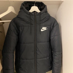 Nike Puff jacka - Säljer min as snygga Nike vinterjacka, då jag har köpt en till liknande.  Jackan har ett band längst nere vid ryggen med Nike loggor.  Har även en Nike logga i fram.   Jätte varm och skön och sitter även lite oversize. Snygg passform.  (Frakt tillkommer på 100 kr)