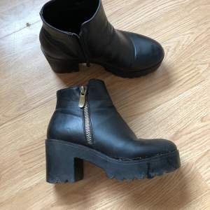 högklackade skor i svart syntetiskt läder med bred klack och både riktig dragkedja + fejk dragkedja som detalj. storlek 39 men är lite stora i storleken. använt skick men inga direkt synliga slitningar, kommer rengöras ordentligt innan du får dem. 