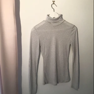  - Vit/grå randig polotröja i stretchigt material. Det är även silvriga sömmar, vilket gör att den glittrar upp och även funkar som ett festligare plagg.