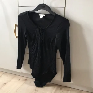  - Svart body med snörning från h&m, långärmad ribbad i blankt tyg   Storlek S (passar XS-S)  Fint skick!