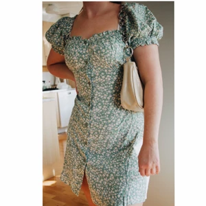 Grönblommig klänning från Nelly - Säljer denna helt oanvända klänningen från Nelly då det inte var min stil! Prislapp finns kvar och bara hängt på en galje sen jag fick den. Den försluts med knappar på framsidan och har en mindre urringning i ryggen! Frakt ingår