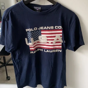Mörkblå ralph lauren t-shirt storlek M (herrstorlek)  - Mörkblå Ralph lauren t-shirt storlek M (herrstorlek). Trycket är lite utslitet. 