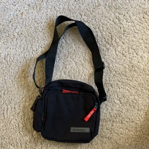 Diesel-väska  - En äkta diesel-väska i nyskick. Svart väska med röda detaljer. Väldigt rymlig med många olika fack. Endast använd en gång. Om ni vill ha fler bilder på den så skicka så fixar jag det. 100 kr + spårbar frakt (70 kr) 💓