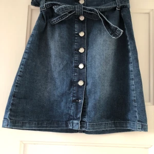 Söt denim, sommarkjol - Em söt denim kjol med knappar där fram och ett bälte man knyter. Frakt ingår ej i pris.