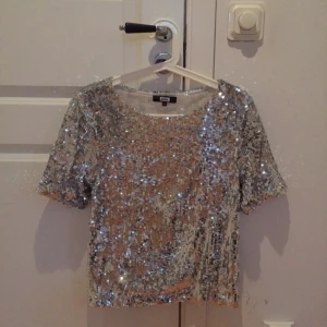  - Supersnygg paljettopp i silver från BikBok. Använd en gång, helt i nyskick. Nypris 300 kr. Passar perfekt till ett par svarta jeans! Kan skicka fler bilder vid intresse!
