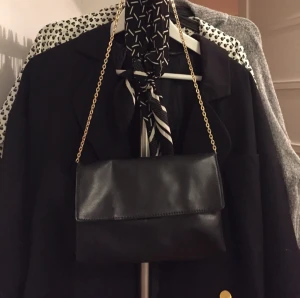  - Väska med guldkedja. Väskan stängs med dragkedja, guldkedjan kan bli såpass lång att du får den över axeln.