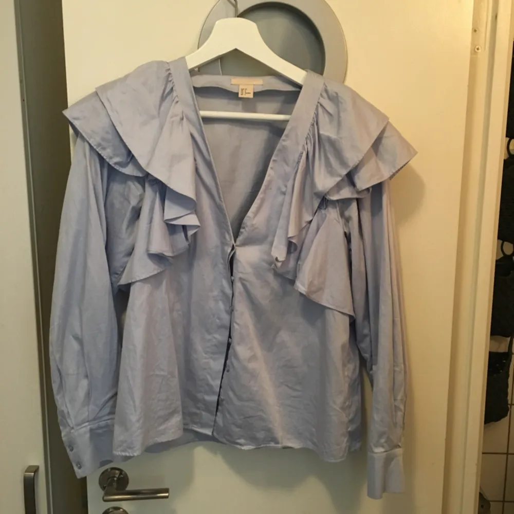 Fin ljusblå skjorta med volang på axlarna. Använd högst 5 gånger. Passar en 36-38. Skjortor.