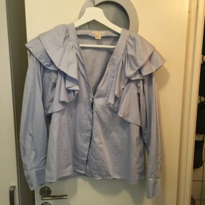  - Fin ljusblå skjorta med volang på axlarna. Använd högst 5 gånger. Passar en 36-38