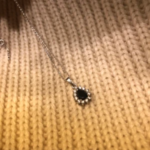 Smycke i silver - Halsband i silver med ett hängsmyckr med blå detalj.