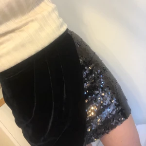 Svart tight kjol med paljetter från Zara - Vad: tight svart kjol från Zara.  Material: 100% polyester. Skick: fint skick, använd 1-2 ggr. Vid noggrann granskning ser man några enstaka trådar som sticker ut längst ned i paljetterna, men det är trådar som håller fast paljetterna och inga lösa trådar så går nog att klippa av om man vill (se närbild).