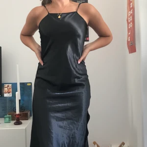 Snygg slipdress från humana  - Svart glansig slip dress köpt second hand på humana! Har två slits på varsin sida och når mig (164cm) strax över knäna. Köparen står för frakten (ca 50kr) eller möts upp i Stockholmsområdet❤️