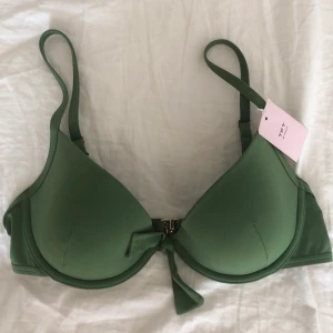 Grön bikiniöverdel - En jättefin grön bikiniöverdel från Twilfit. ALDIRG ANVÄND med lappen kvar. Jättefin grön färg med guldiga detaljer. Köpt för 350kr.