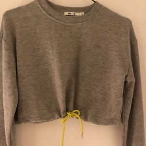 Croppad tröja - Grå croppad tröja från NAKD med gult snöre i midjan! Storlek M 🤍 Aldrig använd!