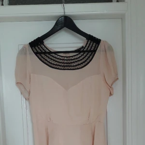  - Drömmig klänning i puderrosa med transparent överdel och halsringning i svart satinspets. Väldigt välsydd med klädda knappar i ryggen och vippig kjol med ett vackert fall. Bara använd ett fåtal gånger, mycket gott skick.