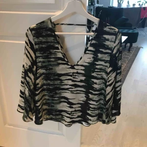  - Tunn blus med mönster. Aldrig använd förutom när bild är tagen. Öppen i ryggen och snygg att stoppa in i byxorna. 100 kr + frakt 39 kr!