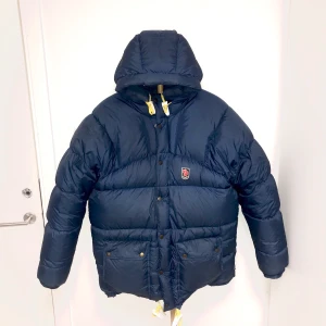 Fjällräven dunjacka-nyskick -  Jackan är fortfarande som ny, utan hål eller fläckar. Storleken är S, modellen är unisex. På mig som är 170 och vanligtvis S/M i strl, är den väldigt stor. Skulle uppskatta jackan som en L/XL. Färg:NAVY. Nypris: ca 6000. Buda från 2000 eller köp direkt för 2600!